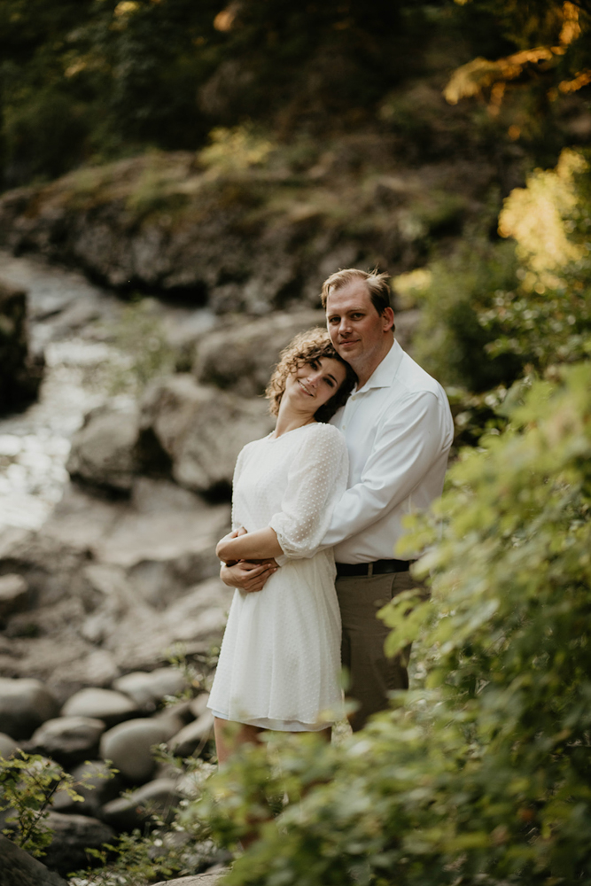 A couple holding each other and smiling by a river at Moulton Falls.