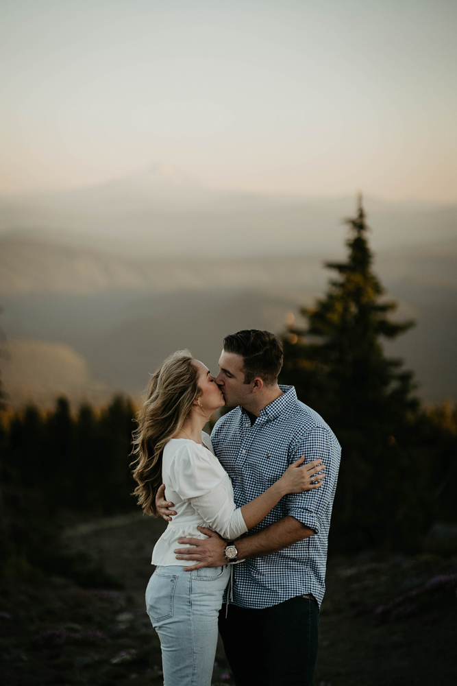 A couple kissing with a pine tree and Mt. Hood in the background at the Timberline Lodge. 