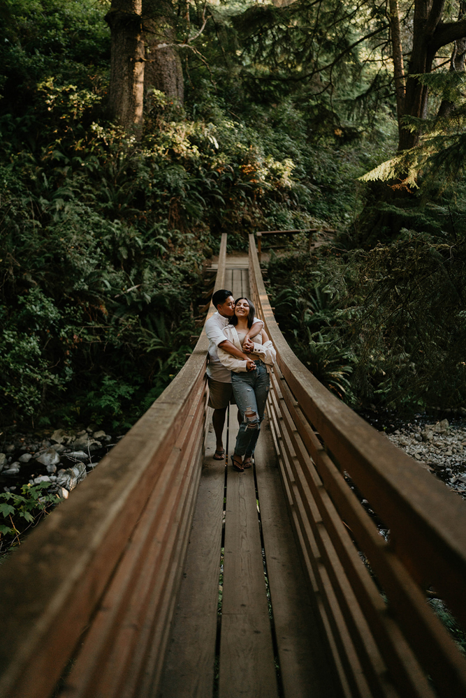 A couple hugging on a bridge in a coastal forest at Short Sand Beach. 
