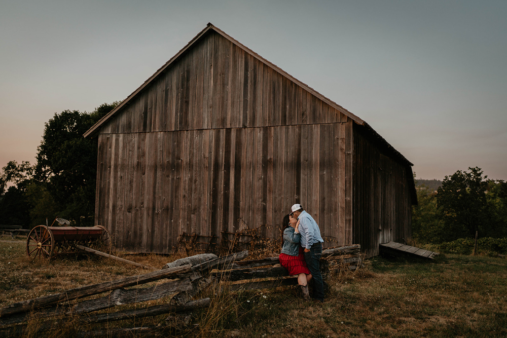 A couple embracing each other in front of the rustic  Manson Barn at Champoeg State Park.