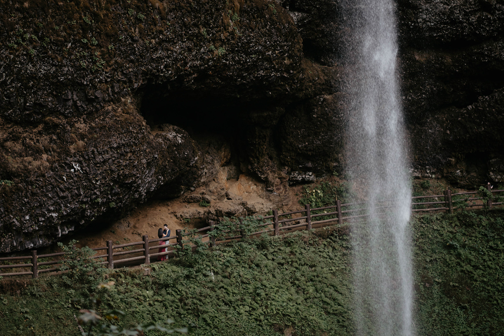 A couple embracing behind a waterfall at Silver Falls. 
