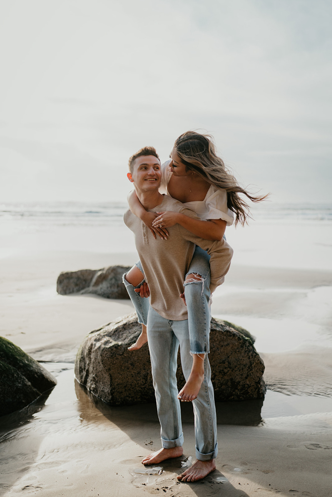 A couple smiling happily at each other with rocks and the beach in the background at Hug Point. 