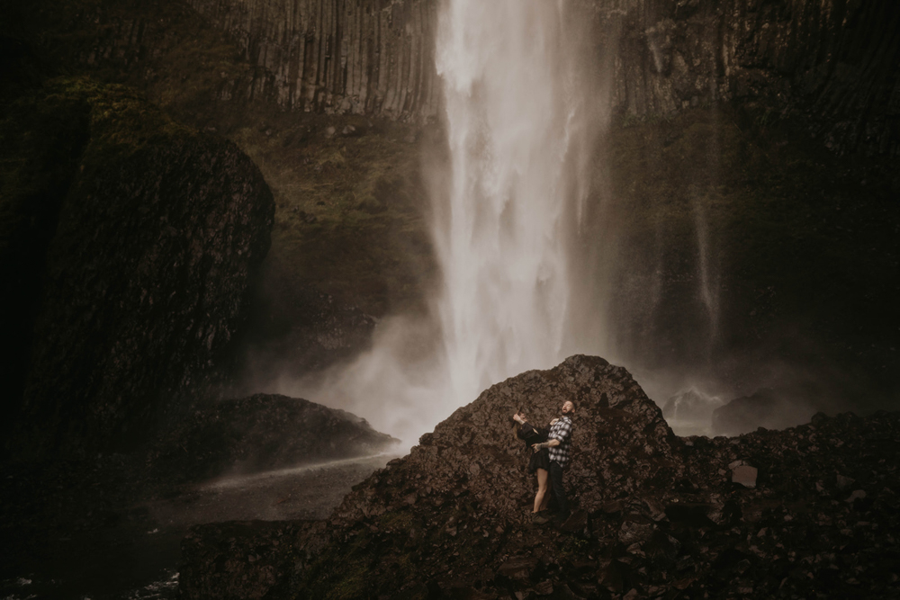 A couple dwarfed by Latourell Falls during the engagement photo shoot. 
