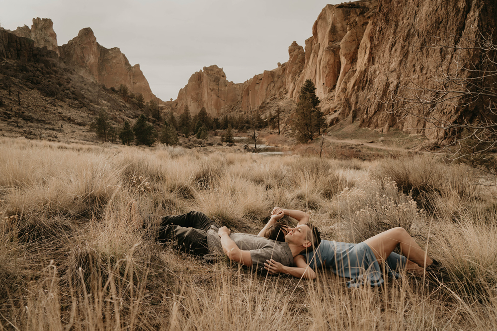 A couple laying in the grass with spires around them at Smith Rock. 