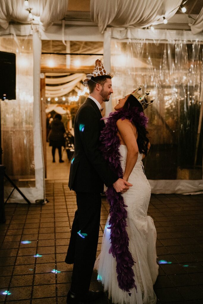 Bride and groom dance while wearing hats and crowns