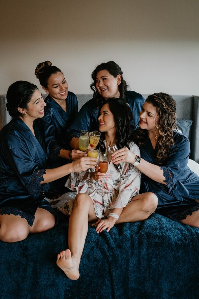 Bride sitting on the hotel bed with bridesmaids wearing navy blue matching robes