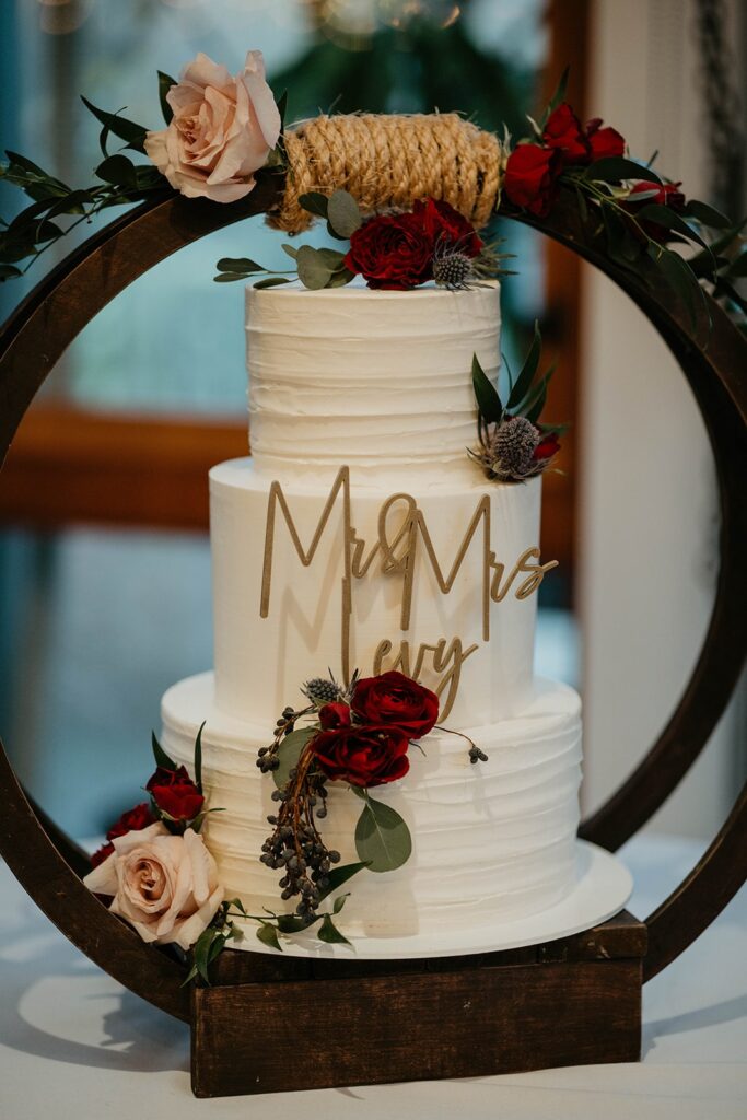 White three tier wedding cake with Mr & Mrs Levy gold sign and red flowers
