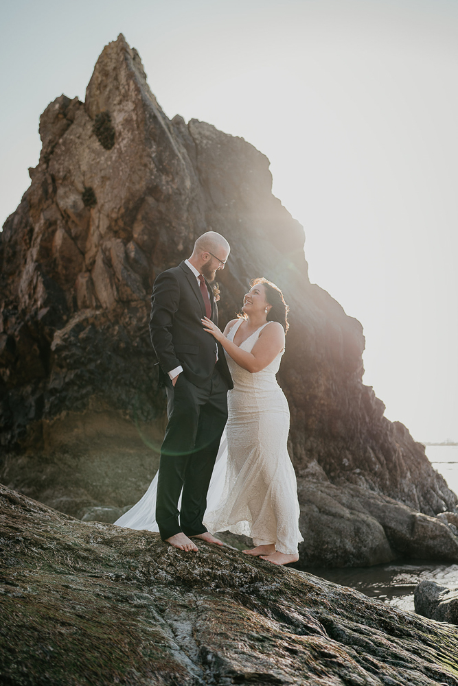 The bride and groom staring into each other's eyes while standing barefoot on a sea stack at Cannon Beach. 
