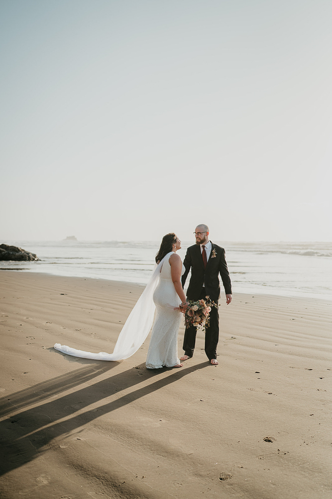 The bride and groom looking lovingly at each other wild standing barefoot in the sand at Cannon Beach. 