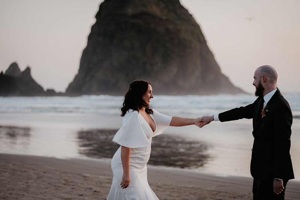 The newlyweds sharing their first dance on the sand, with Haystack Rock in the background as the sun sets over Cannon Beach. 