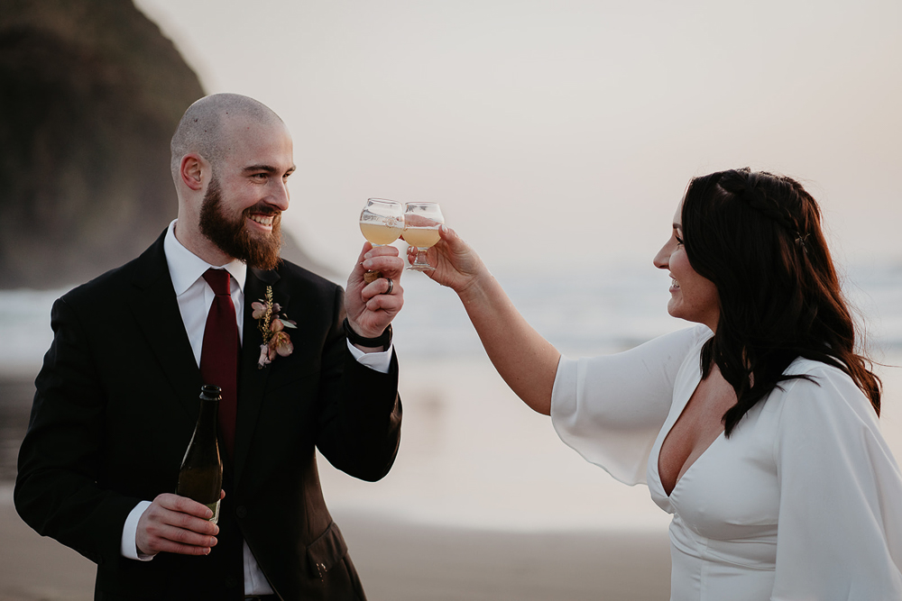 The newlyweds cheersing while the sun sets over Cannon Beach and with Haystack Rock in the background. 