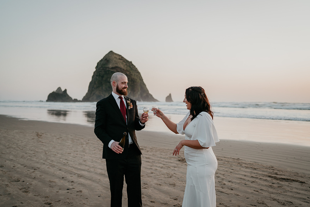 The newlyweds cheersing while the sun is setting at Cannon Beach and with Haystack Rock in the background. 