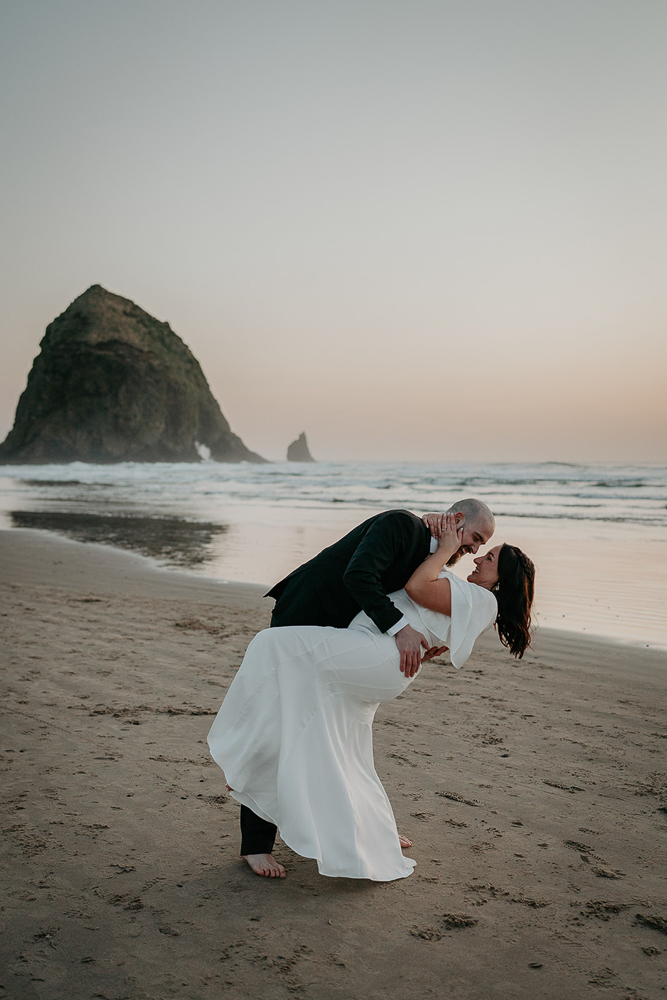 The bride and groom dancing on the sand with the sun setting and Haystack Rock in the background at Cannon Beach. 