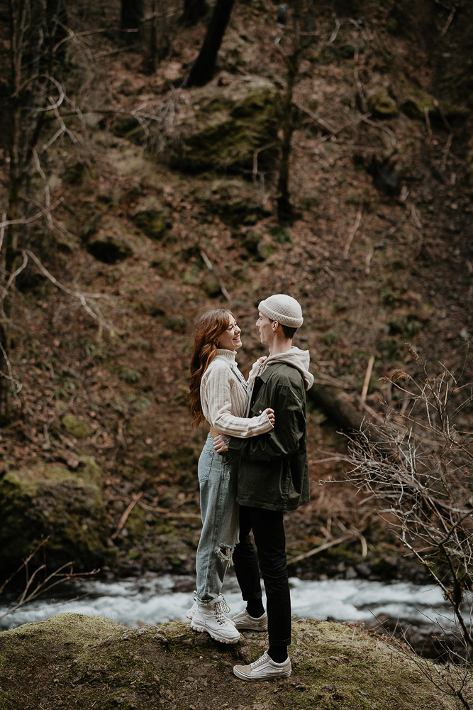 A couple hugging while standing on a boulder with a river in the background at the Columbia River Gorge. 