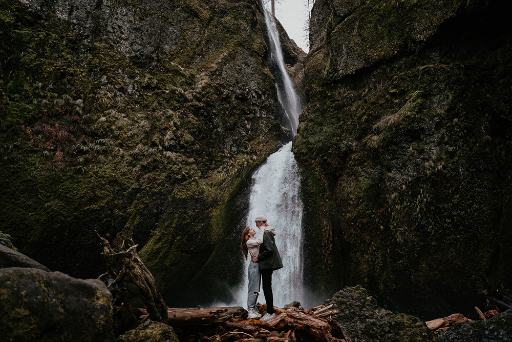 A couple hugging on top of a natural dam with a waterfall in the background at the Columbia River Gorge. 