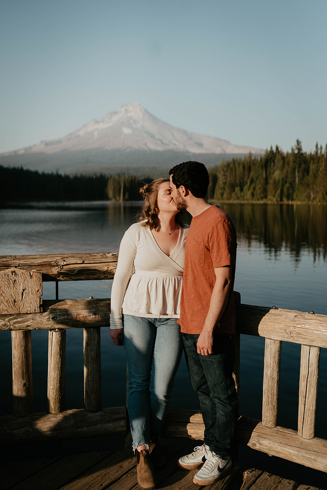 A couple holding kissing on a dock with Trillium Lake and Mt. Hood in the background. 