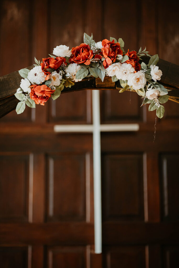 A wedding decoration with flowers and a cross in the background. 