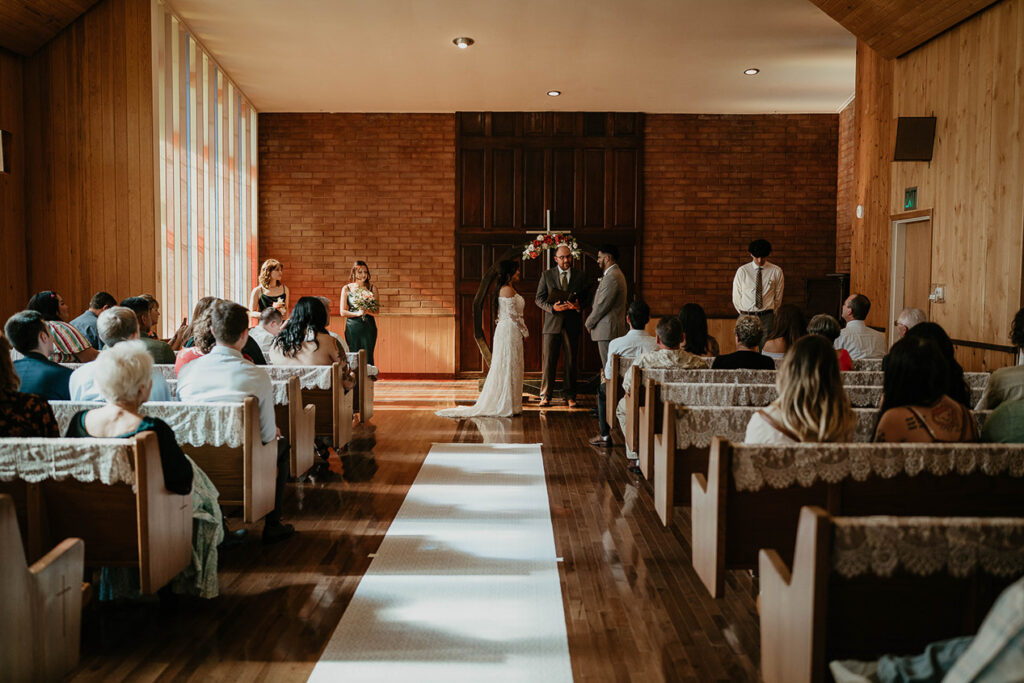 A couple standing at the alter with pews filled with guest to their wedding at Hubbard Chapel.