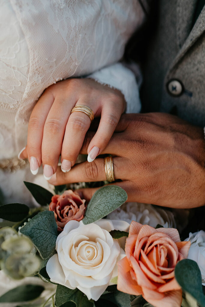 The bride and groom's hand, donning new wedding rings, with the bride's bouquet. 