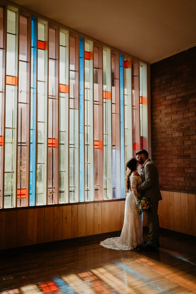 The bride and groom kissing, painted in light from the stained glass window. 