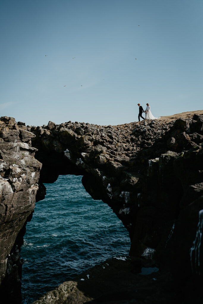 A bride and groom walking over a natural sea-bridge during their Iceland elopement. 