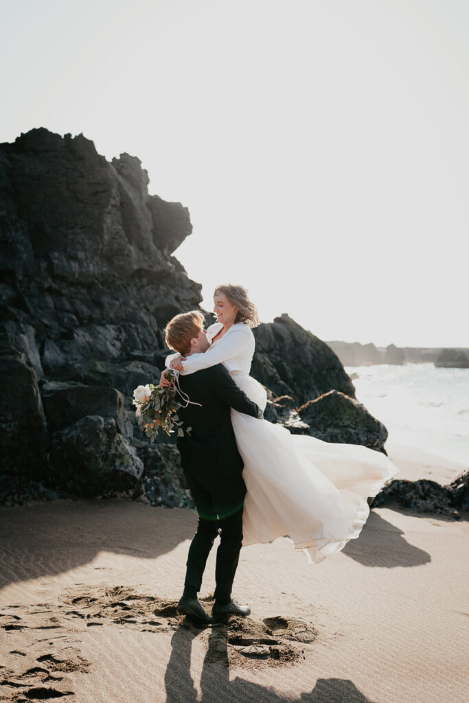 The groom carrying his bride while standing on the beach in Iceland. 