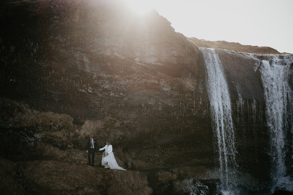 A couple holding hands by a waterfall in Snæfellsnes Peninsula, Iceland. 