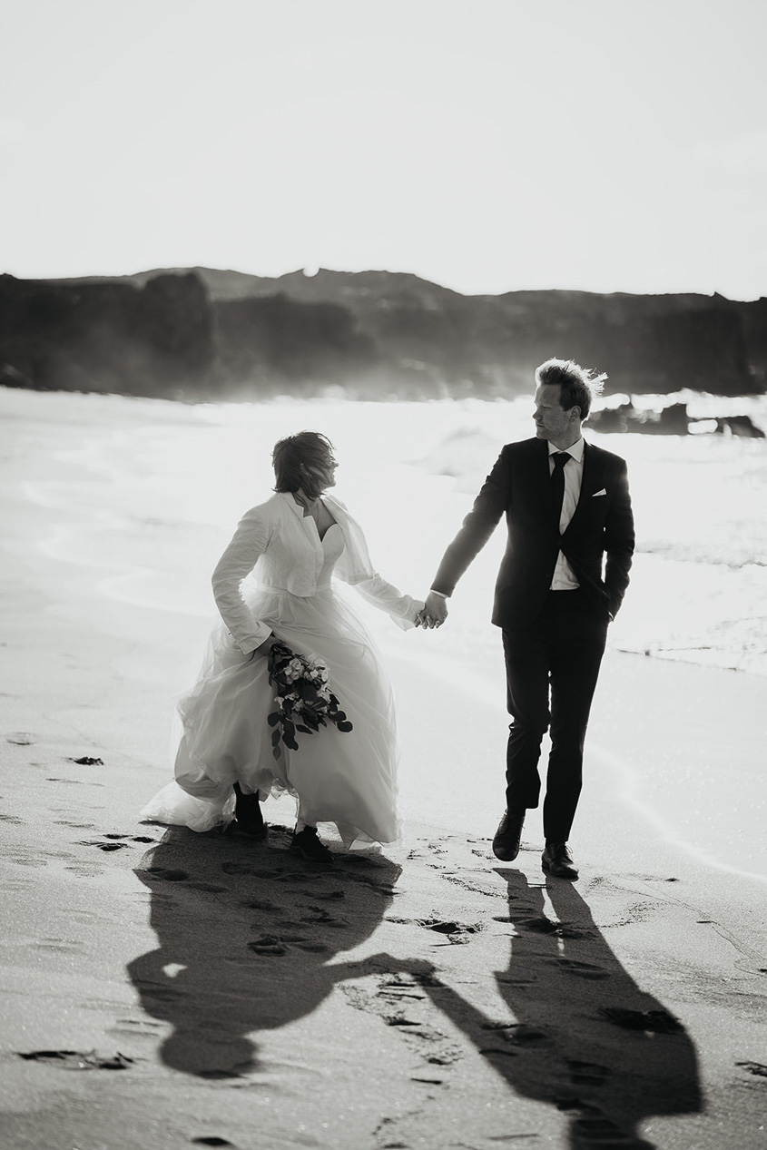 A bride and groom holding hands and walking along the beach along the Snæfellsnes Peninsula in Iceland.