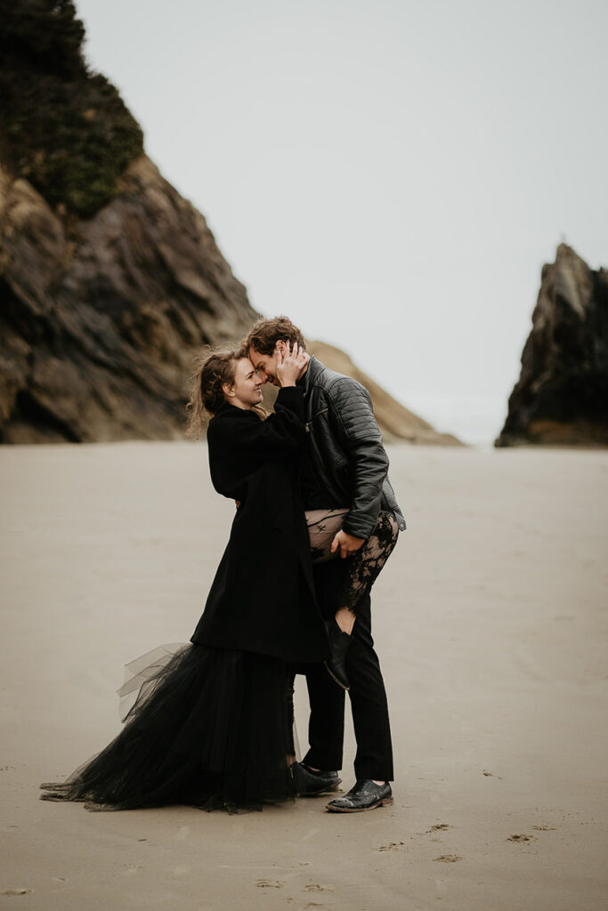 A dressed in black holding each other on the Oregon coast. 