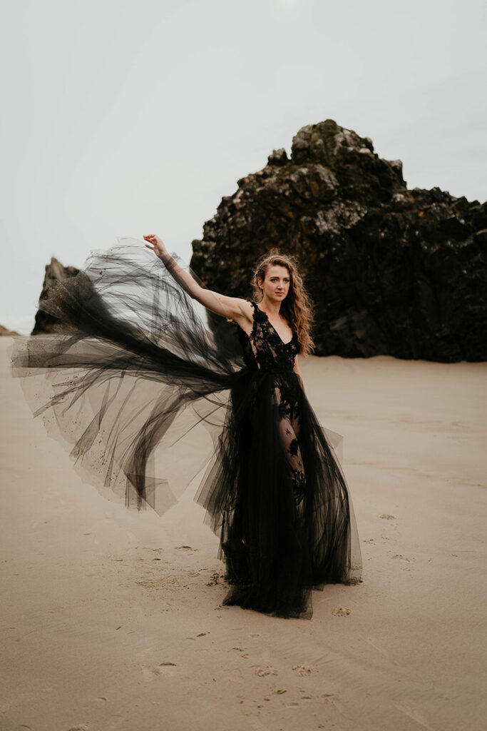 A woman lifting up her veil to let it flow in the wind while standing on the beach. 