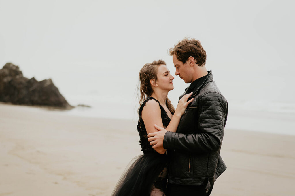 A couple dressed in all black staring into each other's eyes on the Oregon coast. 