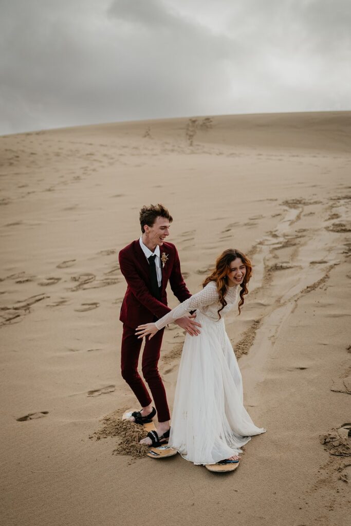 Bride and groom laugh while sand boarding during their adventure elopement in Oregon