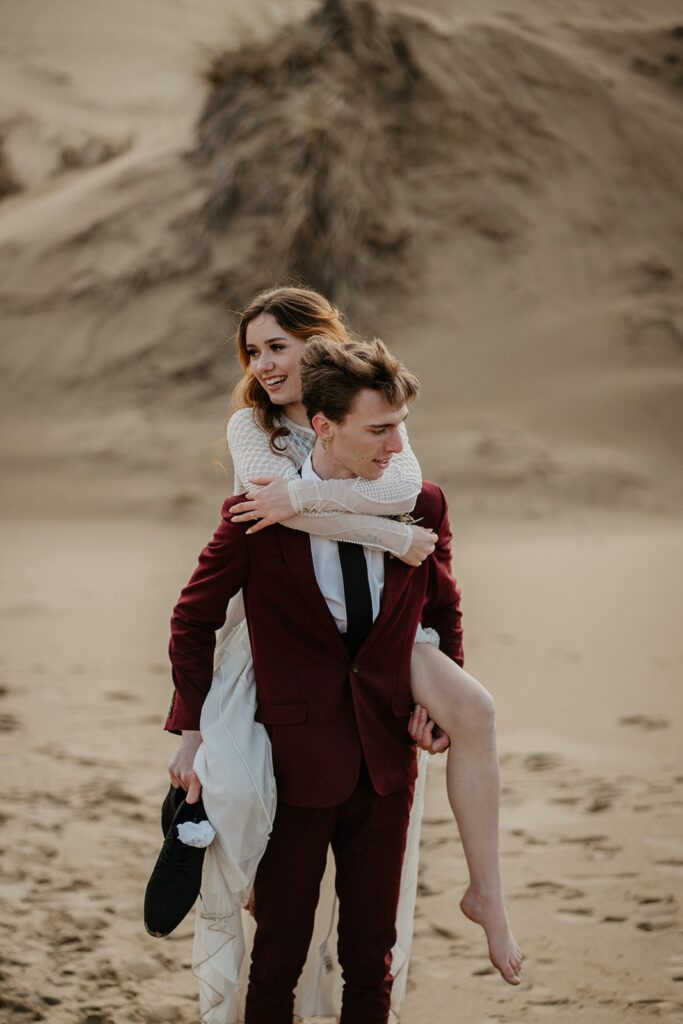 Groom carries bride across the sand dunes during their Oregon elopement 