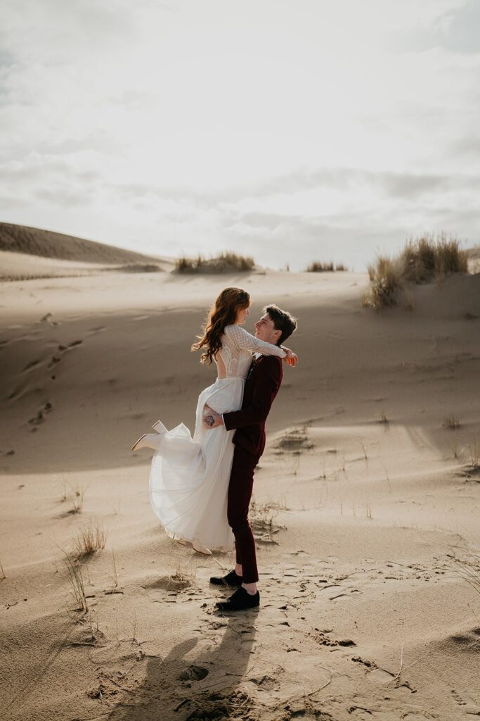 Groom lifts bride into the air during their Oregon sand dunes elopement