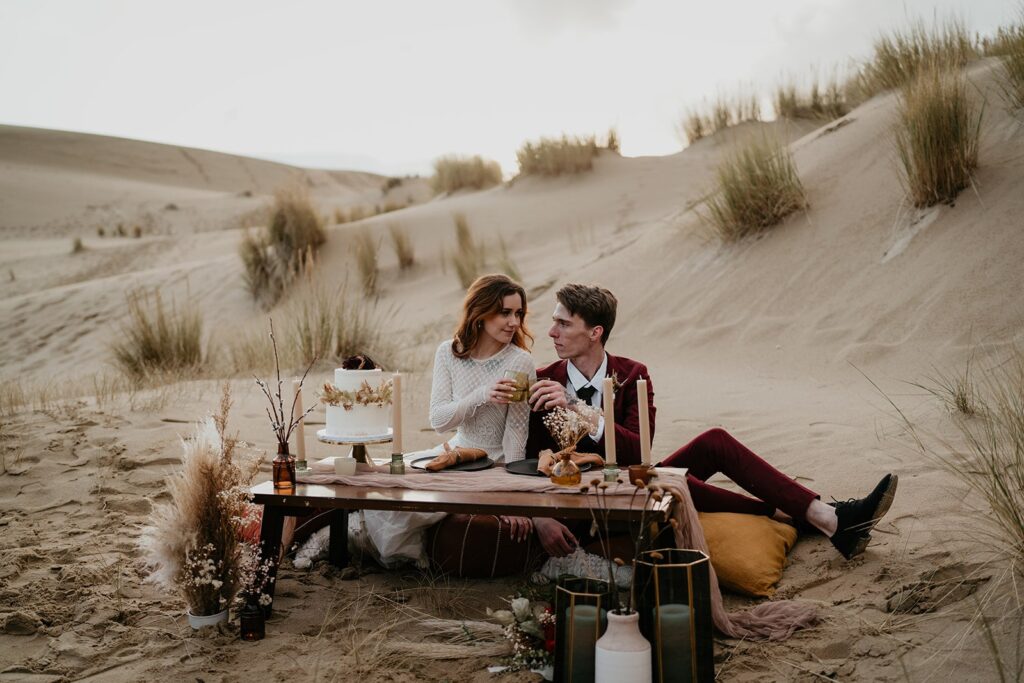 Bride and groom sit at elopement reception table on the Oregon sand dunes
