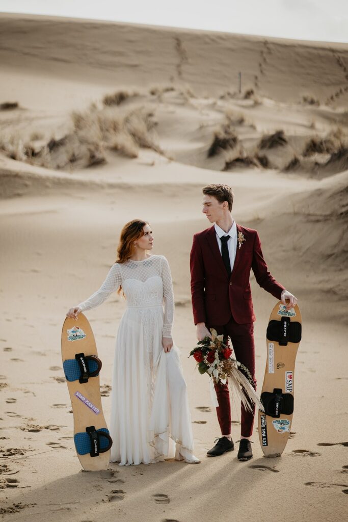 Couple holding sand boards on the sand dunes in Oregon for their adventure elopement