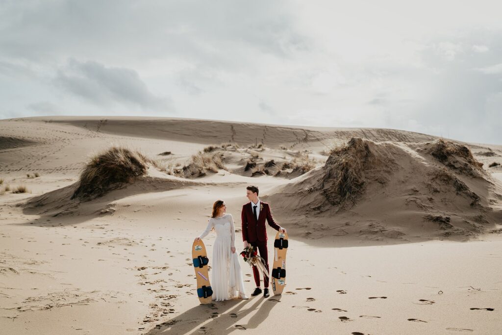 Couple holding sand boards for their Oregon sand dunes elopement photos