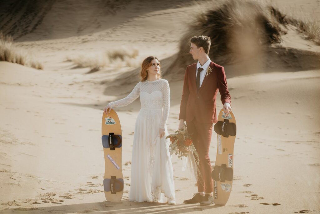 Couple holding sand boards for their Oregon sand dunes elopement photos