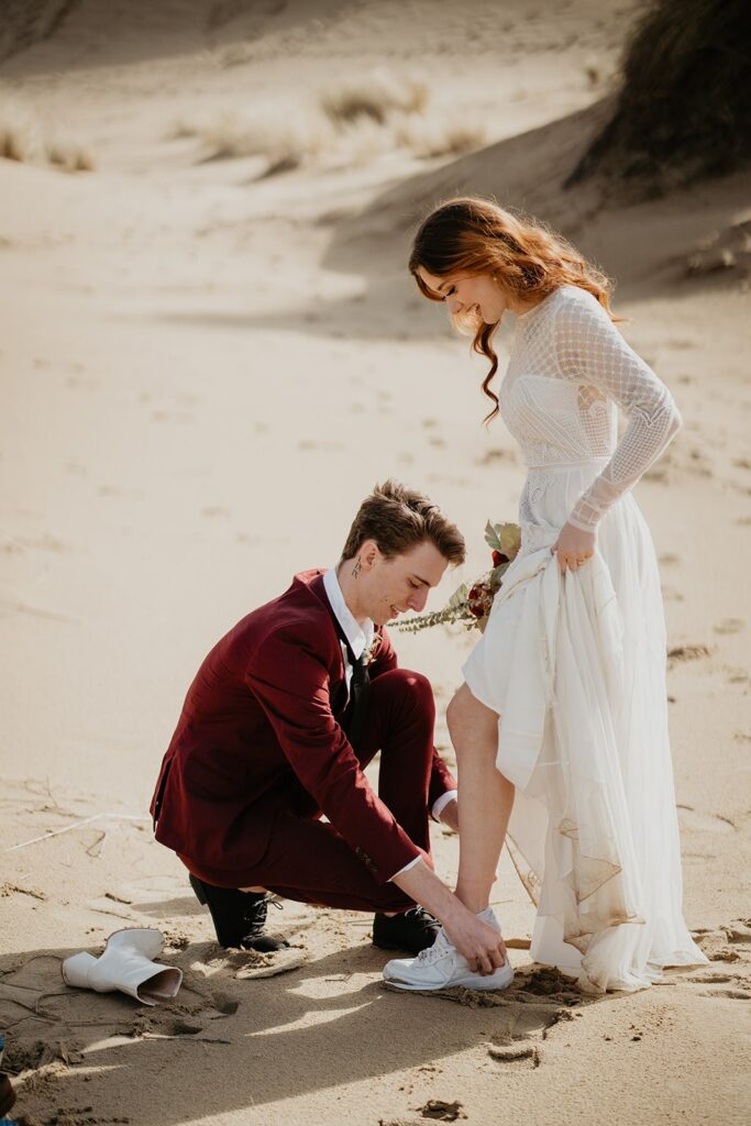 Groom helping bride into shoes for their Oregon sand dunes elopement