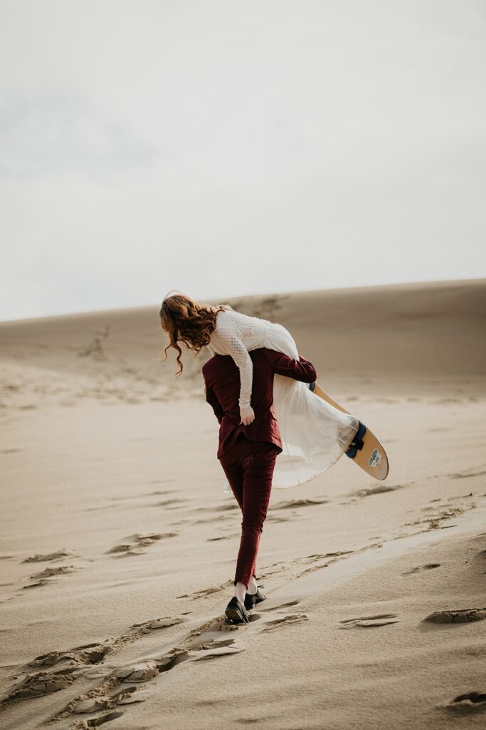 Groom carrying bride across the sand dunes in Oregon