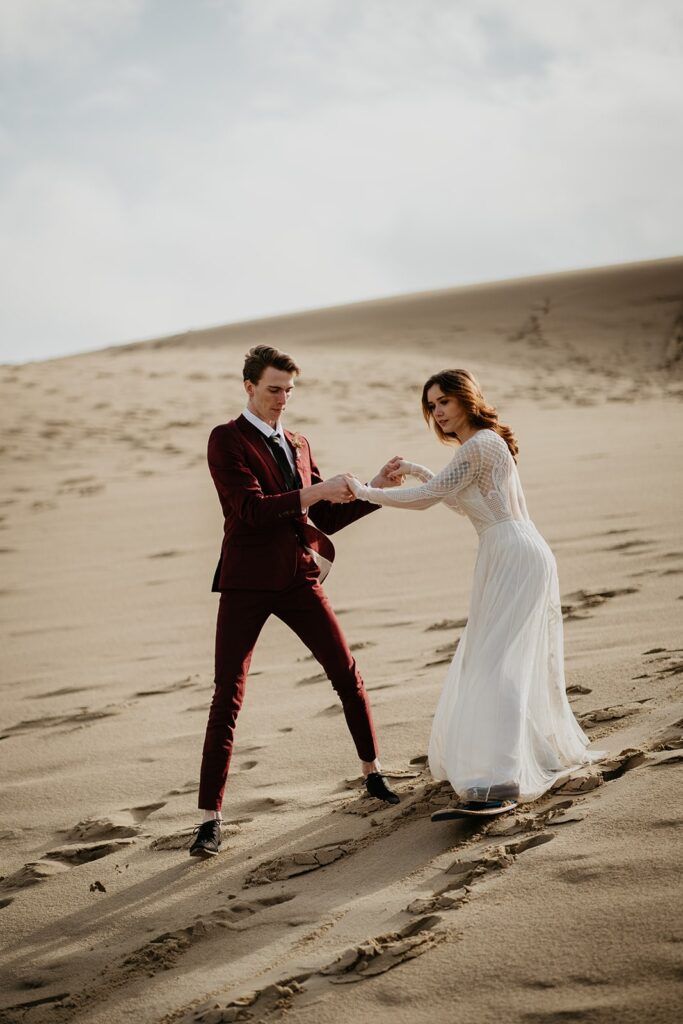 Groom helping bride sand board for the first time during their Oregon sand dunes elopement