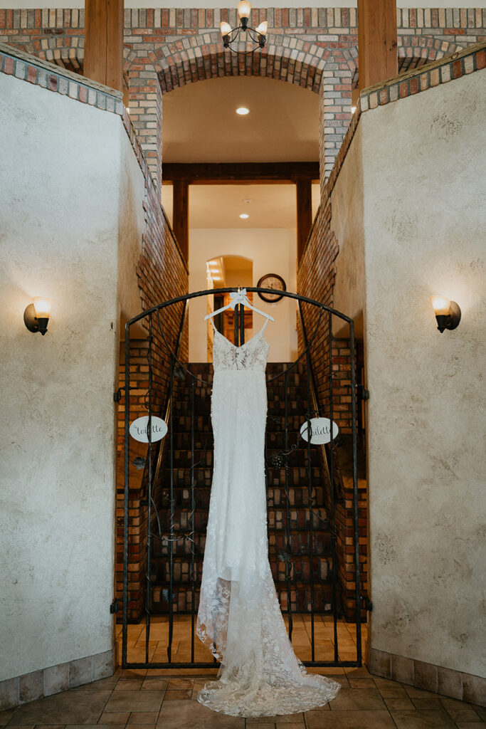A white wedding dress hanging on a gate, with brick stairs leading to a hallway in the background. 