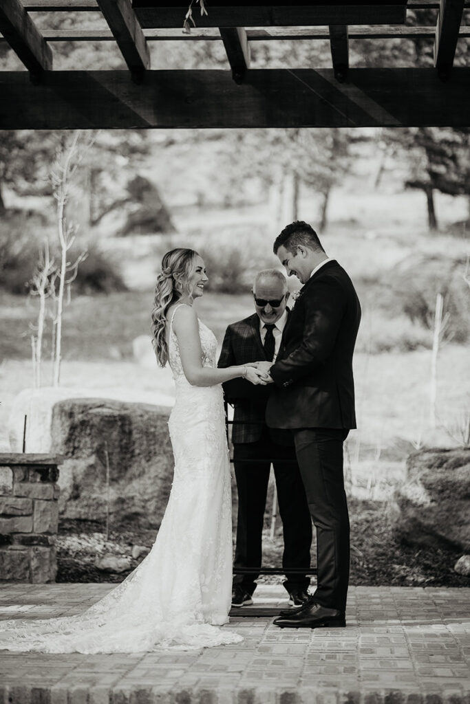 A black and white image of the bride and groom holding hands at the alter. 