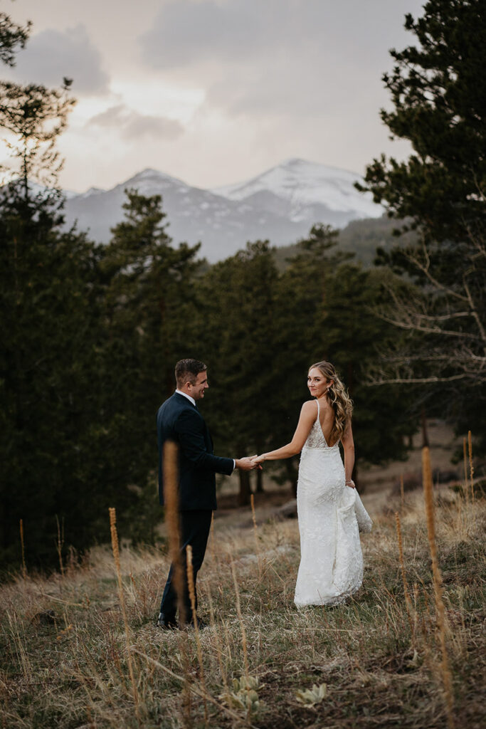 The bride and groom standing in the forest holding hands in Estes Park.