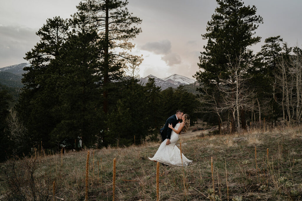 The bride and groom kiss with mountains and forests in the background at Estes Park.