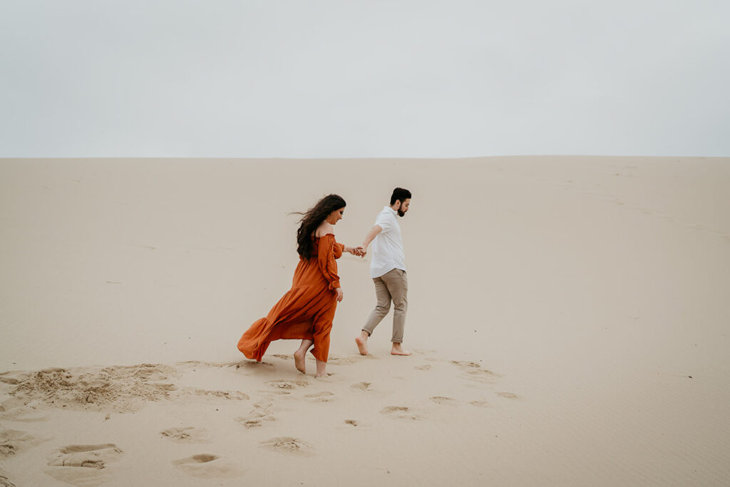 The fiance leading his partner across sand dunes in oregon. 