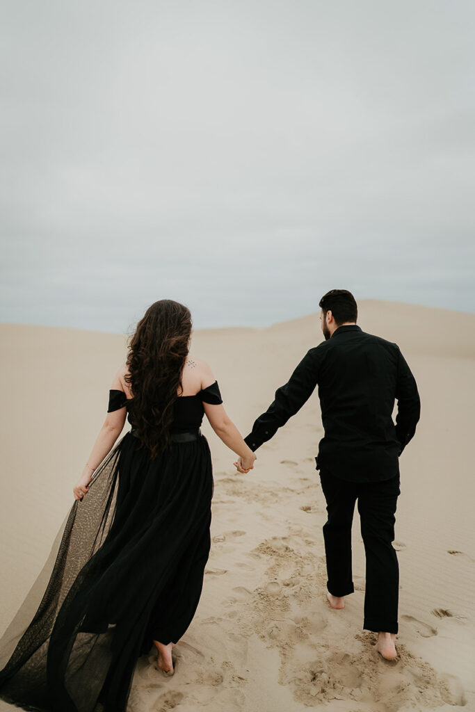 A couple holding hands while walking on the sand dunes in Oregon. 