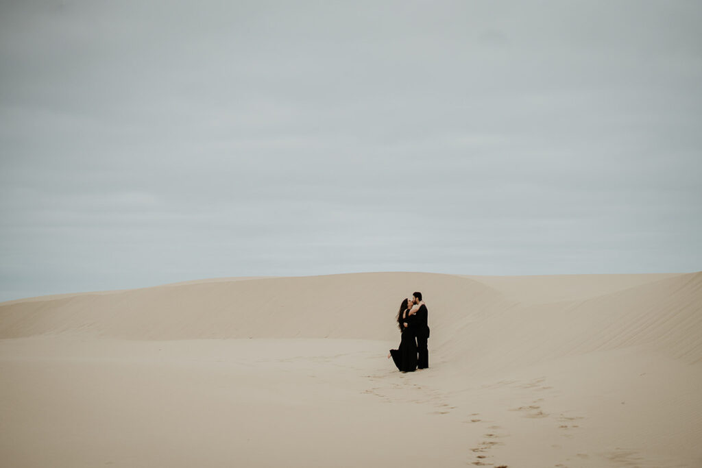 A couple kissing while standing on a sand dune. 