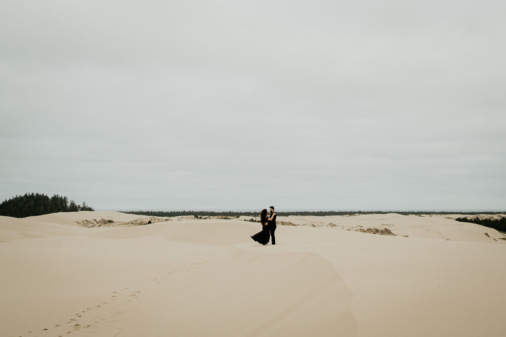 A couple holding each other on a sand dune in Oregon. 