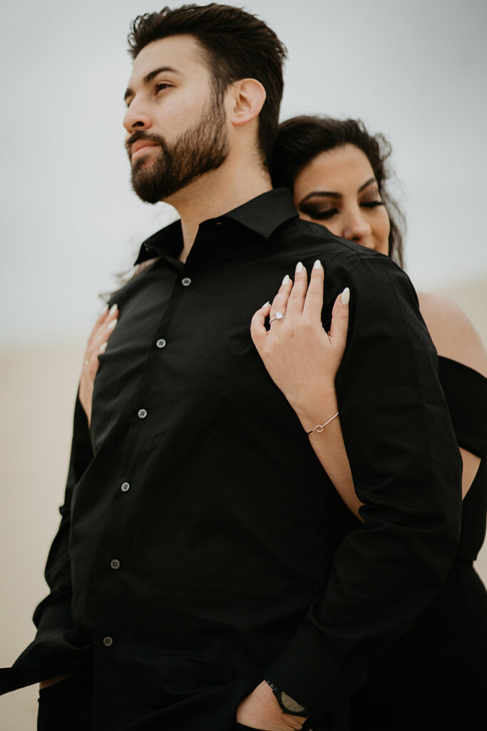 A close up of a girlfriend holding her boyfriend from behind, both dressed in all black. 